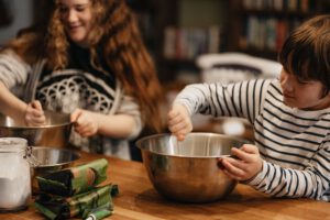 zwei Kinder, ein Junge und ein Mädchen, helfen beim Backen oder Kochen. Sie rühren in Metallschüsseln.